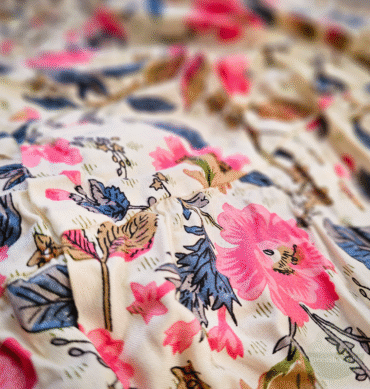 Nahaufnahme des Stoffes eines Boho-Maxirocks mit zartem Blumenmuster in Rosa, Blau und Braun auf cremefarbenem Hintergrund.