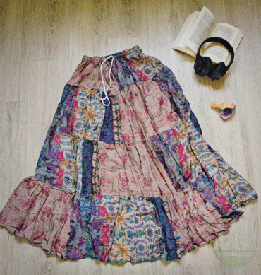 Langer Patchworkrock in Altrosa, Blau und Beige mit floralen Mustern und Rüschen, ausgebreitet auf hellem Holzboden neben Buch und Kopfhörern.