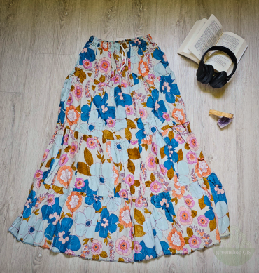 Langer Boho Maxirock mit buntem Blumenmuster in Blau, Pink und Gelb auf hellem Untergrund, gestuft mit Kordelzugbund – flach auf Holzboden neben Kopfhörern und Buch