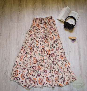 Langer Boho-Rock mit Paisley- und Blumenmuster in Creme, Zimt und Beere, flach auf hellem Holzboden neben Buch, Kopfhörer und Amethyststein
