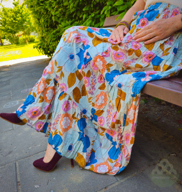 Frau sitzt auf der Bank im bunten Blumenmuster in Blau, Pink und Gelb.